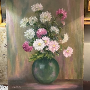 May include: An oil painting on canvas depicting a bouquet of white and pink chrysanthemum flowers arranged in a round, dark green vase. The background features soft, blended strokes of muted green and pink tones. The artist signature Kinman is visible.