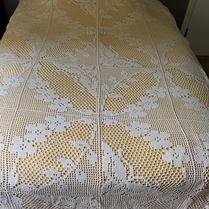 May include: A rectangular crochet bedspread featuring a white floral and leaf pattern created with an openwork mesh stitch. The white crochet work is layered over a solid yellow fabric base, covering the entire surface of the bedspread.