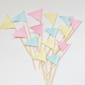 May include: A selection of pastel-coloured triangular flags on wooden sticks. The flags are in shades of pink, yellow, and light blue. The flags are arranged against a white background, creating a cheerful and decorative display.