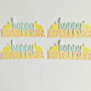 May include: Four pastel-coloured paper cut-outs of bunnies with the text "Happy Easter" in a light blue colour. The bunnies are yellow and the text is on a pink and yellow background.