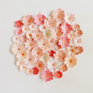 Peut inclure: Une collection de nombreuses petites fleurs en papier superposées dans diverses nuances de rose, de pêche et de corail. Chaque fleur présente une décoration centrale, créant un arrangement circulaire dense de formes florales découpées.