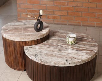 May include: Two round coffee tables with marble tops and dark wood bases. One table has a black vase with decorative branches, and the other has a small candle. The tables are different sizes and are arranged together.