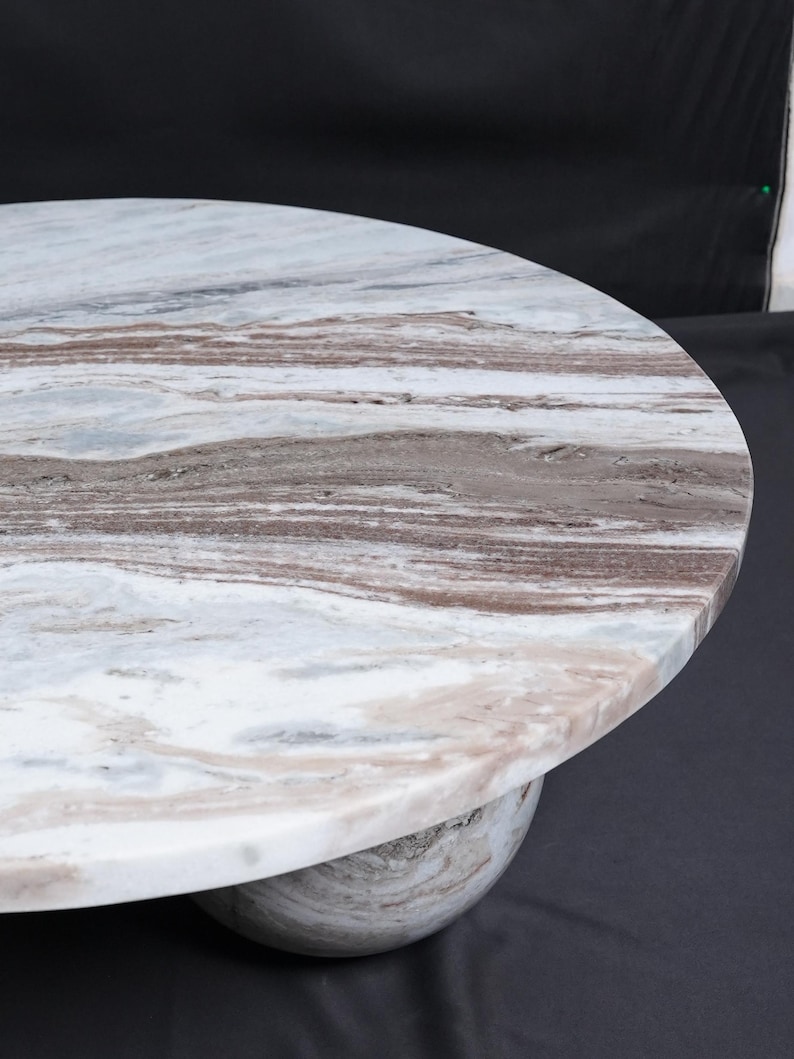 Op de afbeelding: Een ronde marmeren tafel met een wit, bruin en grijs patroon. De tafel wordt ondersteund door een afgeronde basis, wat een modern design cre&euml;ert. De natuursteen heeft een uniek aderingpatroon.