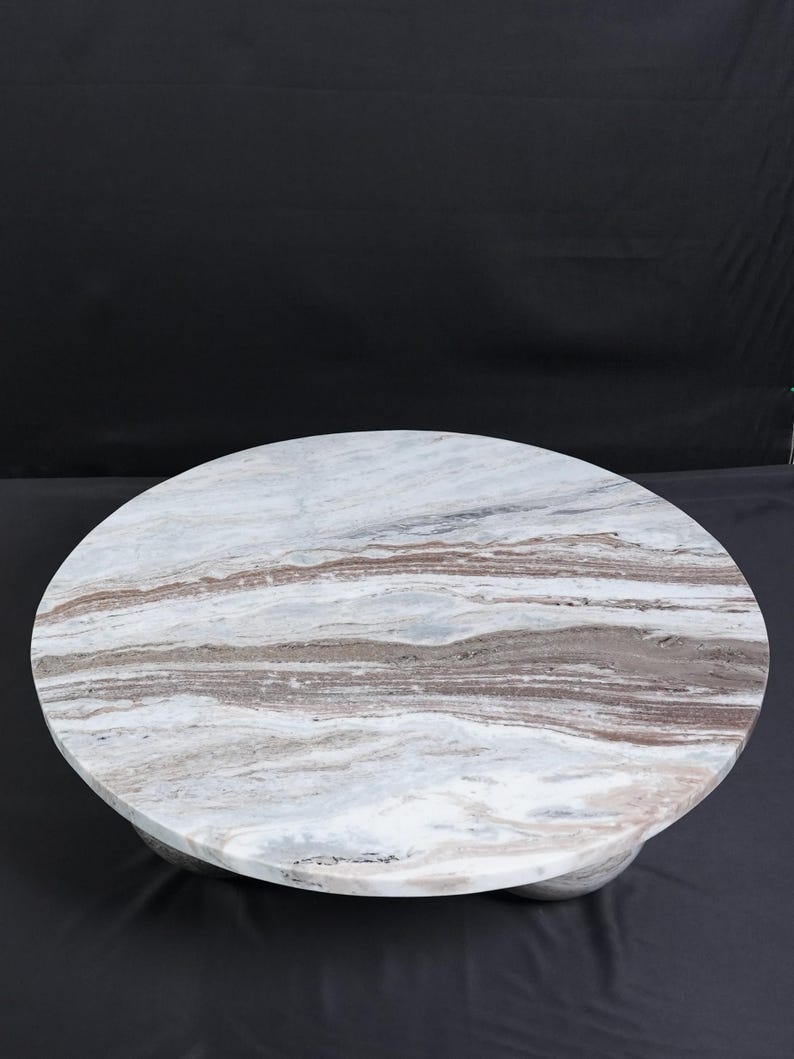 Op de afbeelding: Een ronde marmeren salontafel met een wit, bruin en grijs patroon. De tafel heeft een stevige basis en een glad, gepolijst oppervlak. De tafel heeft een diameter van ongeveer 122 cm.