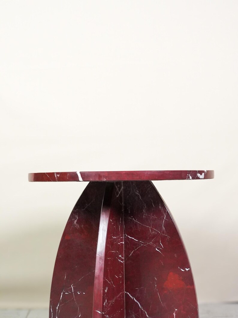 May include: A modern side table with a round top and a curved base. The table is made of red marble with white veining. The table is approximately 20 inches in diameter and 24 inches tall.