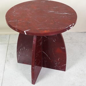 May include: A round, red marble side table with white veining. The tabletop is supported by a pedestal base with three curved legs. The table is approximately 18 inches in diameter and 18 inches tall.
