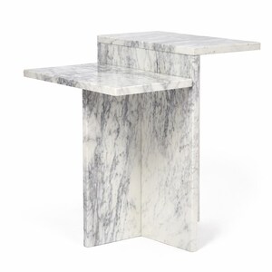 Può includere: Un tavolino moderno in marmo bianco con venature grigie. Il tavolo ha un piano rettangolare e un ripiano inferiore, entrambi sporgenti. La base è una struttura geometrica solida. Misure: circa 61 cm di lunghezza, 30 cm di larghezza e 71 cm di altezza.