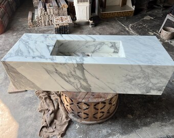 Op de afbeelding: Een witte marmeren wastafel met een rechthoekig bassin. De wastafel staat op een houten standaard met een decoratief patroon.