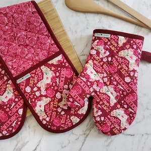 May include: A set of two red oven mitts with a floral pattern and the text "Just a girl who loves chickens" repeated on each mitt.