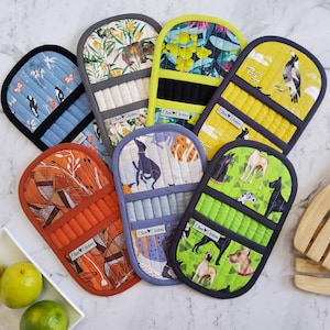 May include: A selection of quilted oven mitts with diverse patterns, such as birds, dogs, and floral motifs. The mitts display a range of colours, including blue, orange, green, and yellow, with black and grey trim. Each mitt is labelled with "Clever Chickens."