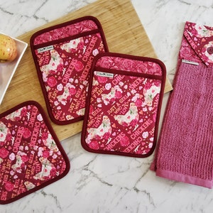 May include: Set of three red and pink floral print pot holders with the text "Just a girl who loves chickens" and a matching red and pink floral print kitchen towel.