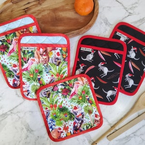 May include: Set of six Christmas-themed pot holders. Three pot holders feature a white background with a colourful design of Australian animals wearing Santa hats. The other three pot holders feature a black background with a white design of kangaroos wearing Santa hats.
