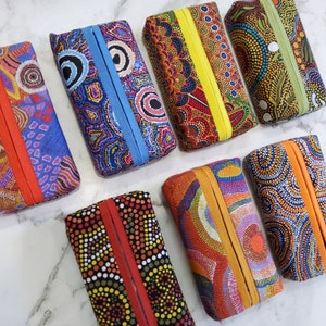 May include: Ten tissue boxes featuring colourful Aboriginal art designs. The boxes are made of fabric and have a flap that opens to reveal the tissues. The designs feature geometric patterns and bright colours, including red, blue, yellow, and green.