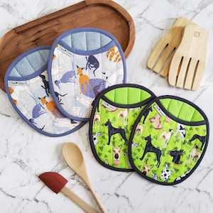 以下が含まれることがあります： 青、緑、白の犬柄のキルティングオーバル鍋つかみ。木製のサラダサーバー、木のスプーン、赤いヘラも存在します。鍋つかみは青または黒のトリムが付いています。