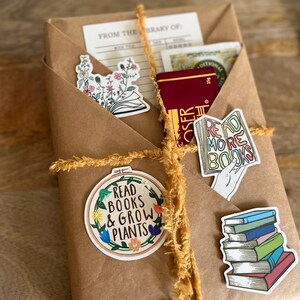 Peut inclure: Un colis en papier kraft envelopp&eacute; de ficelle jaune et d&eacute;cor&eacute; de diff&eacute;rents autocollants. Les autocollants pr&eacute;sentent des illustrations de fleurs, de livres et le texte "Read Books & Grow Plants".