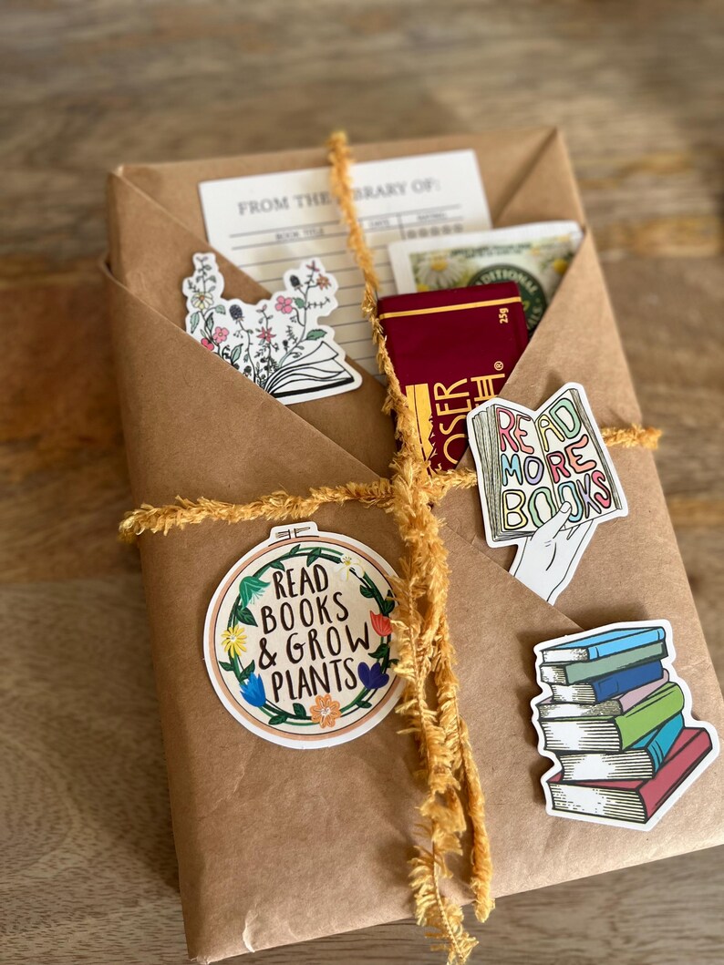 Peut inclure: Un colis en papier kraft envelopp&eacute; de ficelle jaune et d&eacute;cor&eacute; de diff&eacute;rents autocollants. Les autocollants pr&eacute;sentent des illustrations de fleurs, de livres et le texte "Read Books & Grow Plants".