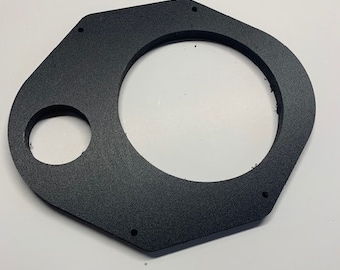 May include: Black speaker mounting ring with a smaller circular cutout. The ring has a hexagonal shape and several small holes around the edge.