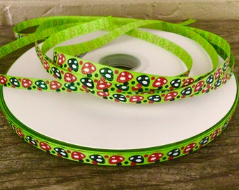 May include: A spool of lime green grosgrain ribbon featuring a repeating pattern of glittery red and dark blue mushrooms with white spots. The ribbon is wound around a white plastic core, displaying a continuous print of small fungi.