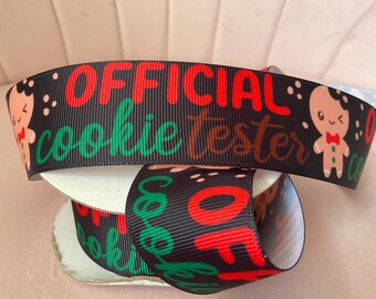 May include: A black grosgrain ribbon featuring the red text OFFICIAL and green cursive text cookie tester, interspersed with cartoon gingerbread characters wearing red bow ties, all printed on a textured fabric spool for holiday crafting.