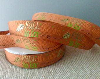 May include: Orange ribbon with the text "Fall is in the air" in gold lettering and green accents. The ribbon is folded and stacked on top of itself.