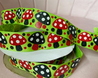 May include: A spool of lime green grosgrain ribbon featuring a repeating pattern of red and black mushrooms with white spots. The mushroom caps are decorated with a subtle glitter finish, and the ribbon is wound around a circular cardboard core.