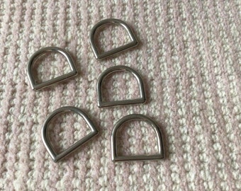May include: Five silver metal D-rings on a pink and white textured surface.