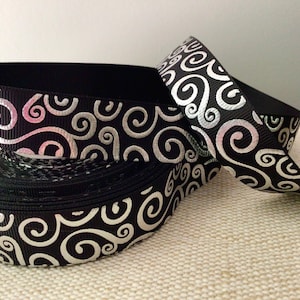 May include: Black ribbon with a silver swirl pattern. The ribbon is rolled up and tied in a bow.