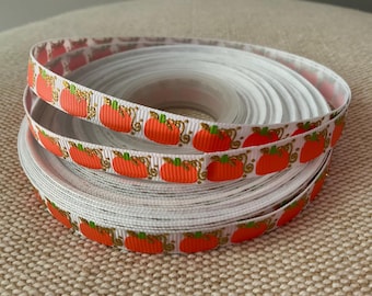 May include: White ribbon with orange pumpkins and gold accents. The ribbon is rolled up and the pumpkins are visible on the outside of the roll.