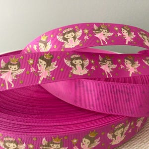May include: A roll of bright pink ribbon featuring a repeating pattern of cartoon fairies with gold accents. The fairies are depicted with wings, crowns, and wands. The ribbon is made of a textured material.