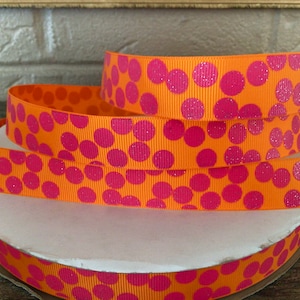 May include: Orange ribbon with pink polka dots. The polka dots have a glittery finish.