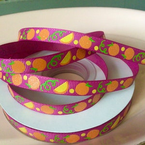 May include: A spool of pink ribbon with a repeating pattern of orange citrus fruit and green leaves.