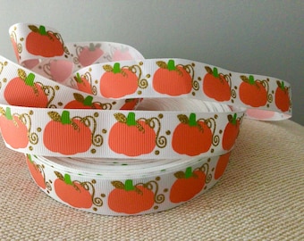 May include: White ribbon with a repeating pattern of orange pumpkins with green stems and gold glitter swirls.