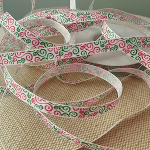 May include: White ribbon with a repeating pattern of red and green swirls. The ribbon is spooled and scattered, creating a decorative element. The ribbon is likely used for gift wrapping or crafting.