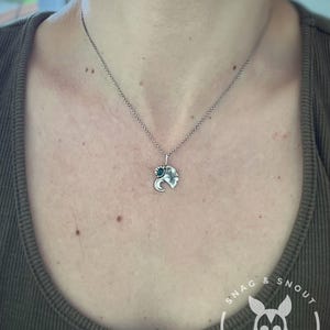 K&ouml;nnte beinhalten: Silberfarbene Halskette mit einem Anh&auml;nger in Form eines Elefantenkopfes mit einem kleinen t&uuml;rkisfarbenen Akzent. Der Anh&auml;nger h&auml;ngt an einer filigranen Kette. Die Person tr&auml;gt ein gr&uuml;nes Oberteil.