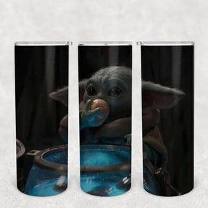 May include: Three stainless steel tumblers with a black background and a green alien character eating a small orange object. The alien is sitting in a blue container.