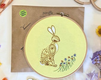Könnte beinhalten: Ein gelber Stickrahmen mit einem braunen Hasenmuster und blau-weißen Blumen. Auf der Verpackung ist der Text "paraffle" zu sehen, sowie der Hinweis "100% organic fabric".