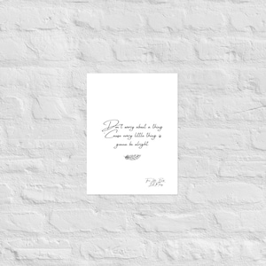 May include: A white poster with the quote "Don't worry about a thing, cause every little thing is gonna be alright" in black script. A small feather illustration is below the quote. The poster is displayed against a white brick wall.