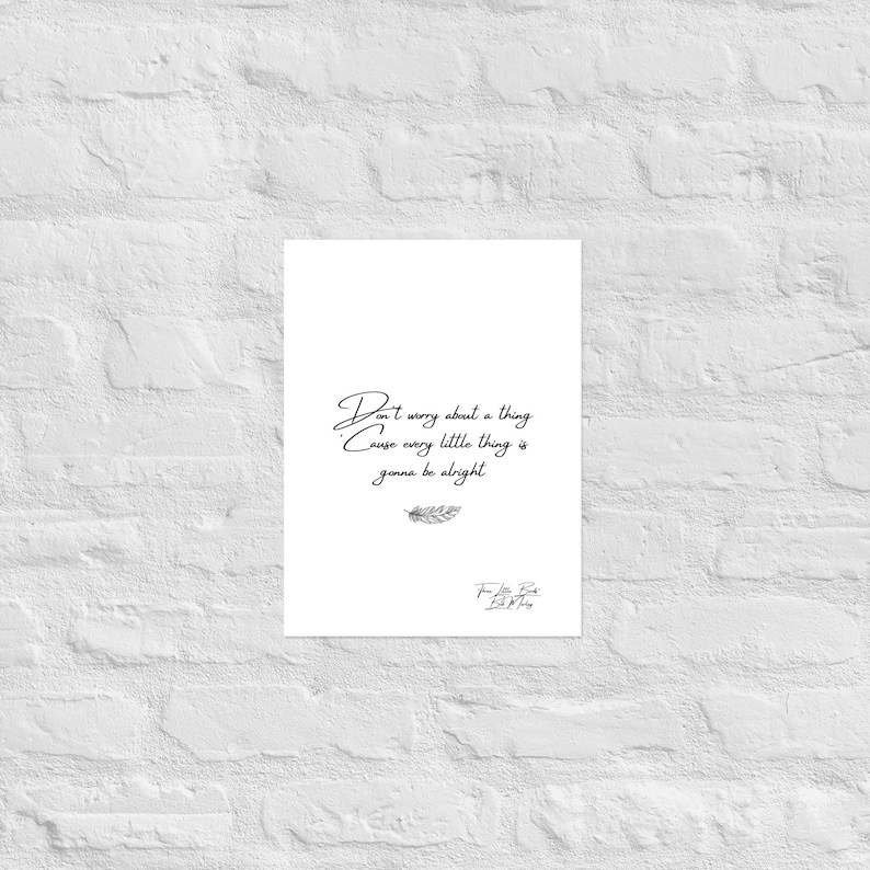 May include: A white poster with the quote "Don't worry about a thing, cause every little thing is gonna be alright" in black script. A small feather illustration is below the quote. The poster is displayed against a white brick wall.