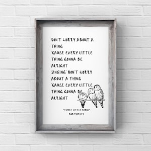 May include: A framed print with the lyrics "Don't Worry About a Thing" and "Three Little Birds" by Bob Marley. The print features a black and white illustration of three birds perched on a branch. The frame is a light gray color.