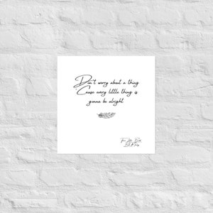 May include: A white square print with the text "Don't worry about a thing Cause every little thing is gonna be alright" in black script. A small feather illustration is below the text. The print is against a white brick wall.