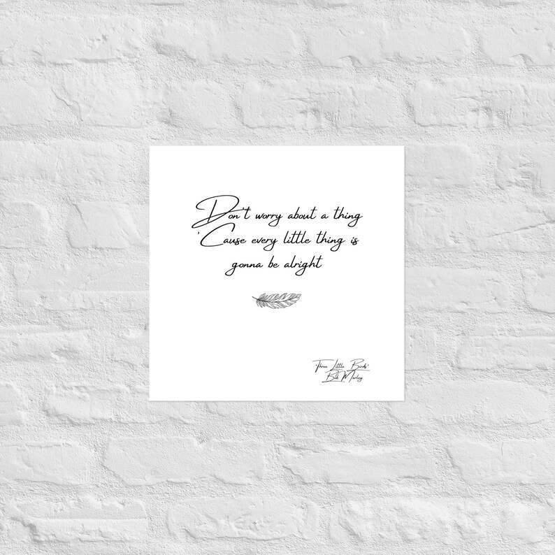 May include: A white square print with the text "Don't worry about a thing Cause every little thing is gonna be alright" in black script. A small feather illustration is below the text. The print is against a white brick wall.