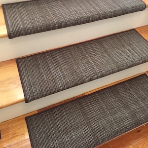 May include: A set of four stair treads with a woven, textured appearance. The treads are primarily dark gray with lighter gray and white threads, and have a dark brown border. They are installed on wooden stairs.