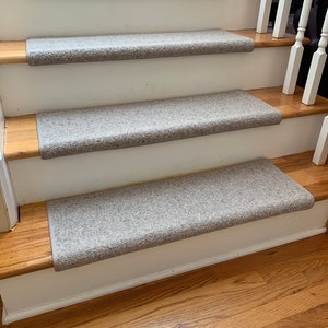 May include: Close-up of a set of beige carpet stair treads on wooden stairs. The treads are a light beige color and have a textured surface. The stairs are made of wood and have a natural finish.