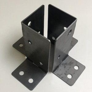 May include: Two metal post brackets with multiple holes for attaching to a wooden post. The brackets are made of steel and have a dark gray finish.