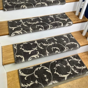 May include: Four stair treads with a dark gray background and a white, swirling floral pattern. The treads are rectangular and sit on wooden steps with white risers. The treads add a decorative and safe element to the staircase.