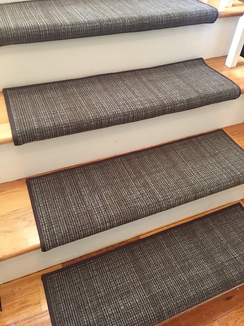 May include: A set of four stair treads with a woven, textured appearance. The treads are primarily dark gray with lighter gray and white threads, and have a dark brown border. They are installed on wooden stairs.