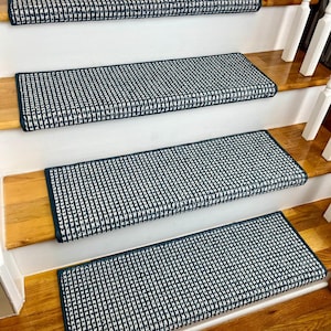 May include: Four blue and white patterned stair treads with a dark blue border. The treads are on a wooden staircase with white risers.