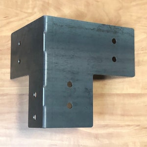May include: A black metal corner brace with multiple holes for attaching to wood. The brace is designed to reinforce corners and provide structural support.