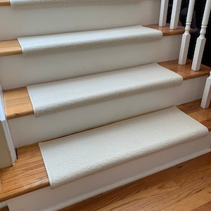May include: Beige carpet stair treads on wooden stairs with white painted risers. The treads are a soft, plush material and are designed to provide traction and comfort.