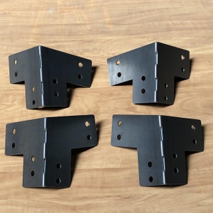May include: Four black metal corner brackets with multiple holes for attaching to wood. The brackets are designed to reinforce corners and provide support.